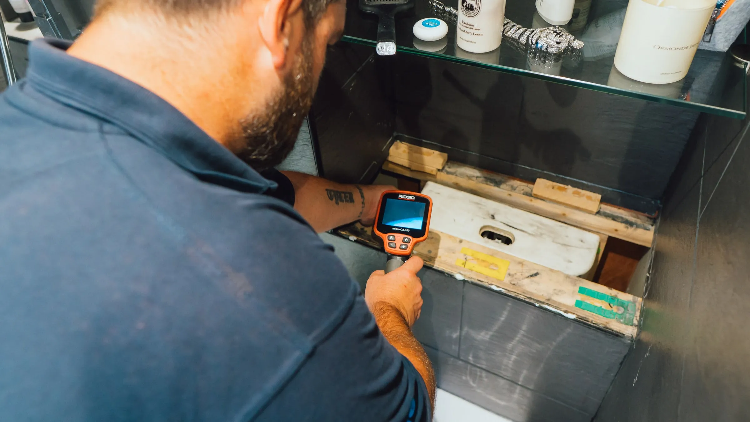 Engineer pointing a thermal camera at the pipework behind a removed bathroom cabinet panel