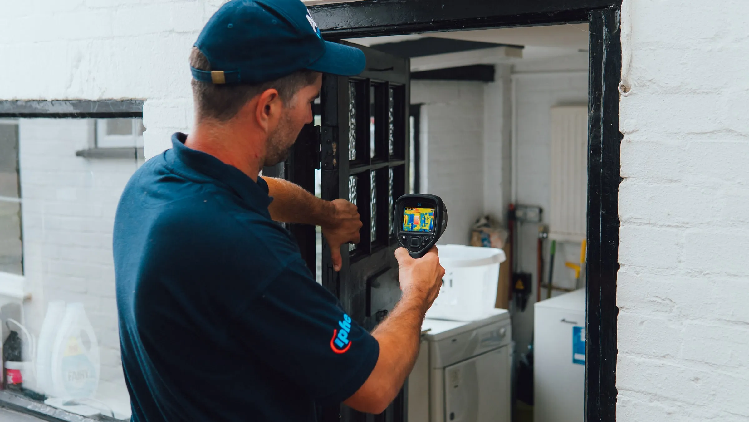 Engineer holding a thermal camera up to the doorway of a utility room with a washing machine and tumble dryer inside