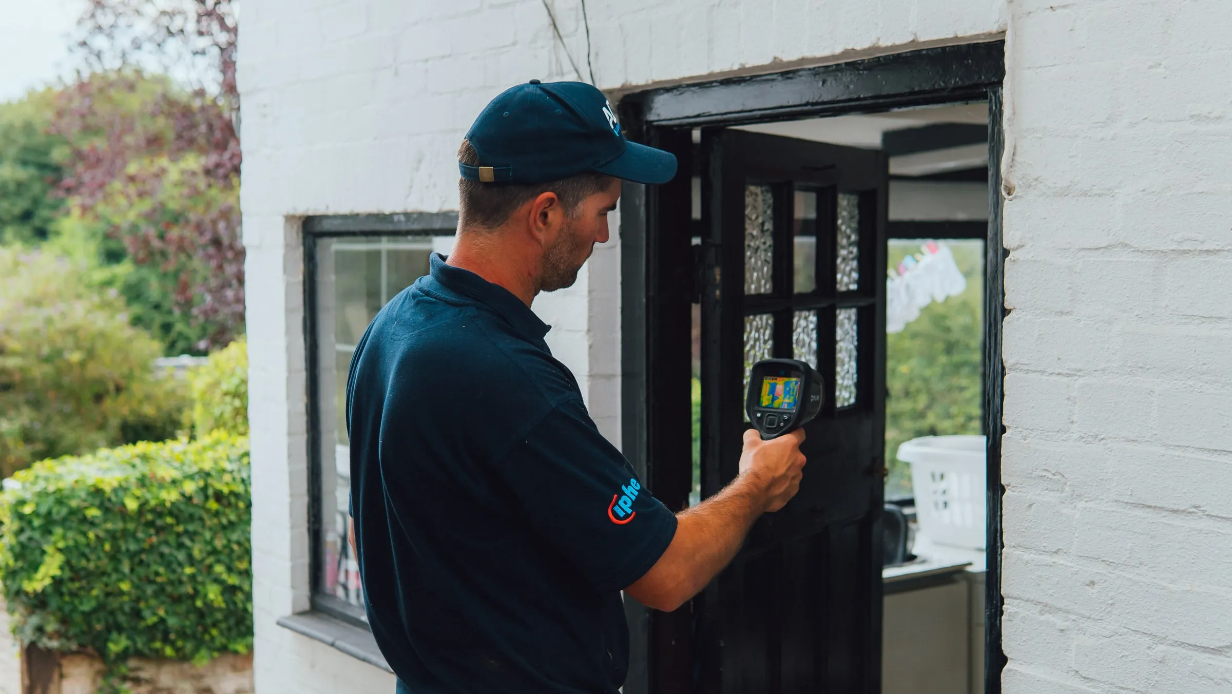 Engineer checking the frame of a back door in a white-painted brick wall with a thermal camera