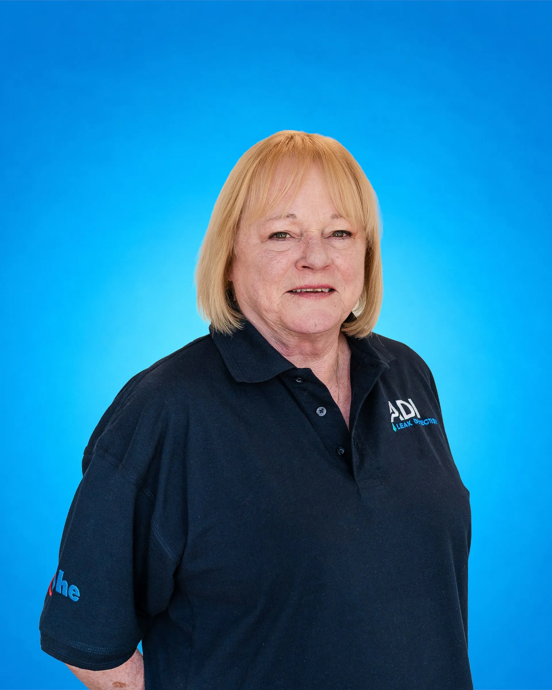 Member of ADI's office team in an ADI polo shirt, photographed against a blue backdrop