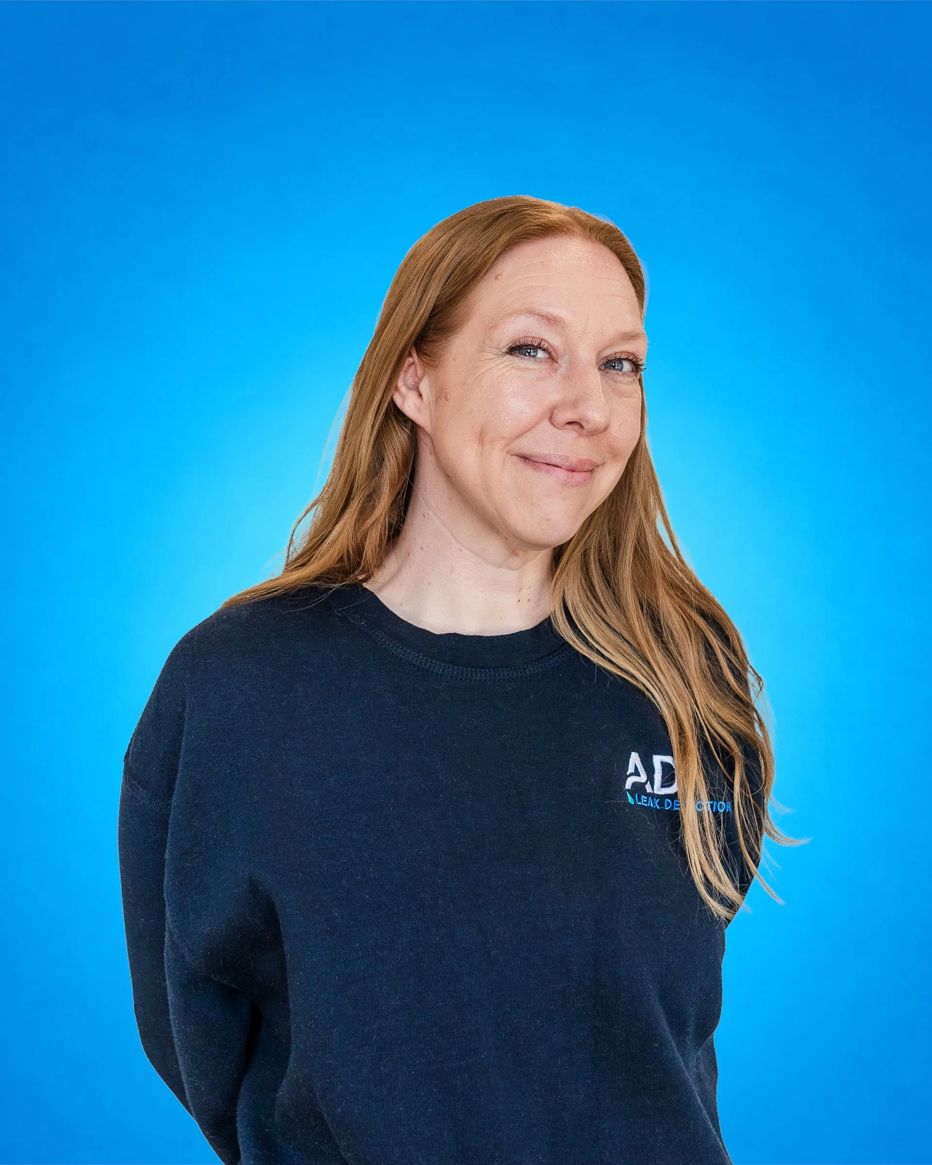 Member of ADI's office team in an ADI sweatshirt, smiling, photographed against a blue backdrop