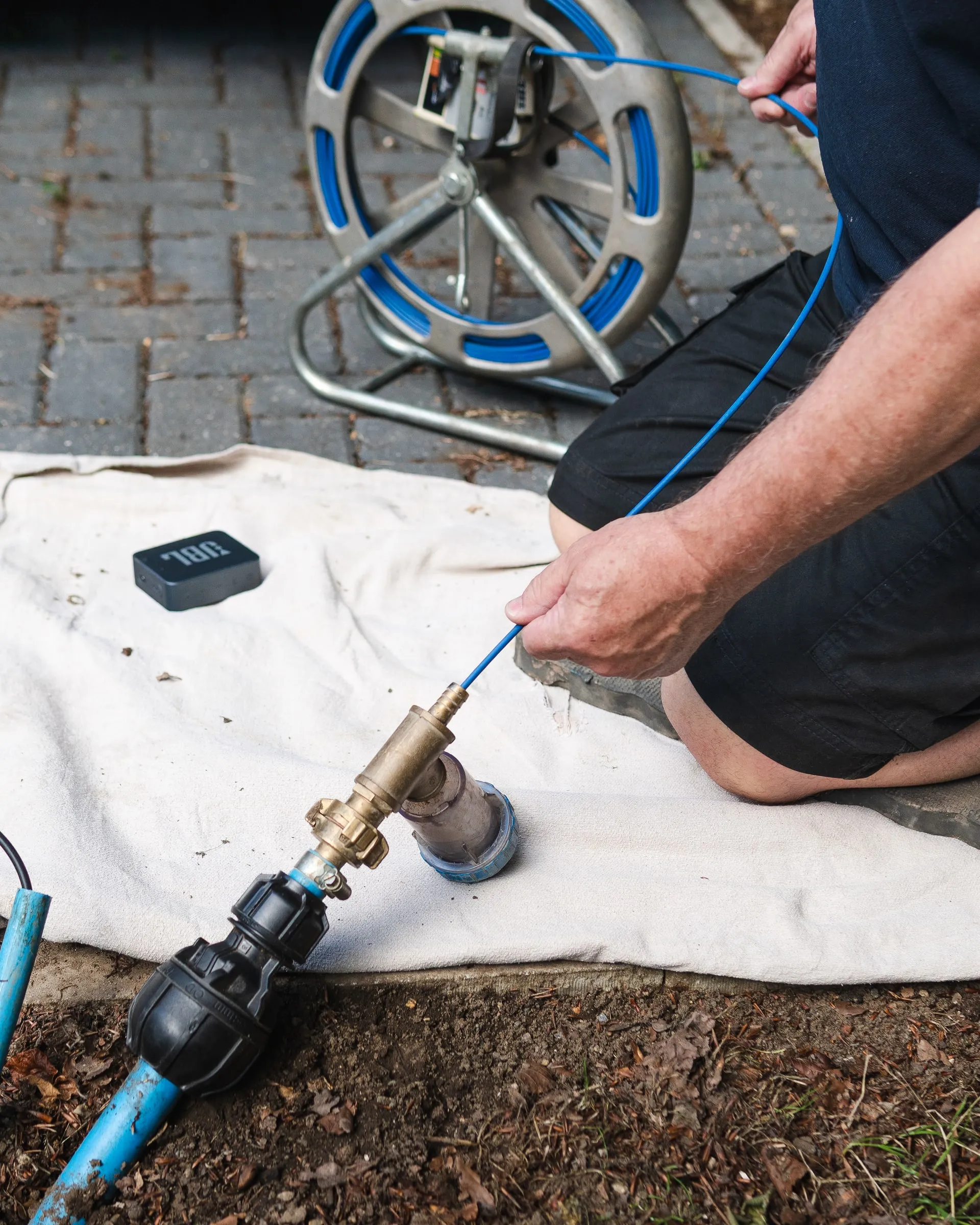 Engineer fitting a brass test connector to a blue plastic water pipe laid on a dust sheet